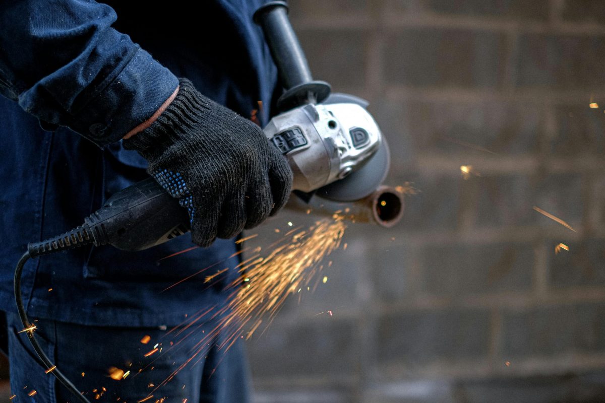 Worker using angle grinder for metalwork, generating bright sparks indoors.